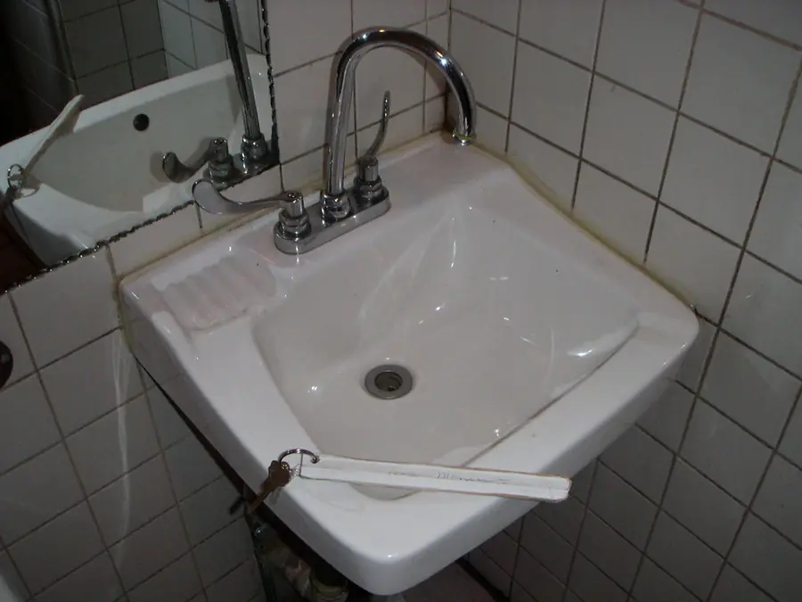 A white wash basin and tap on a tiled wall
