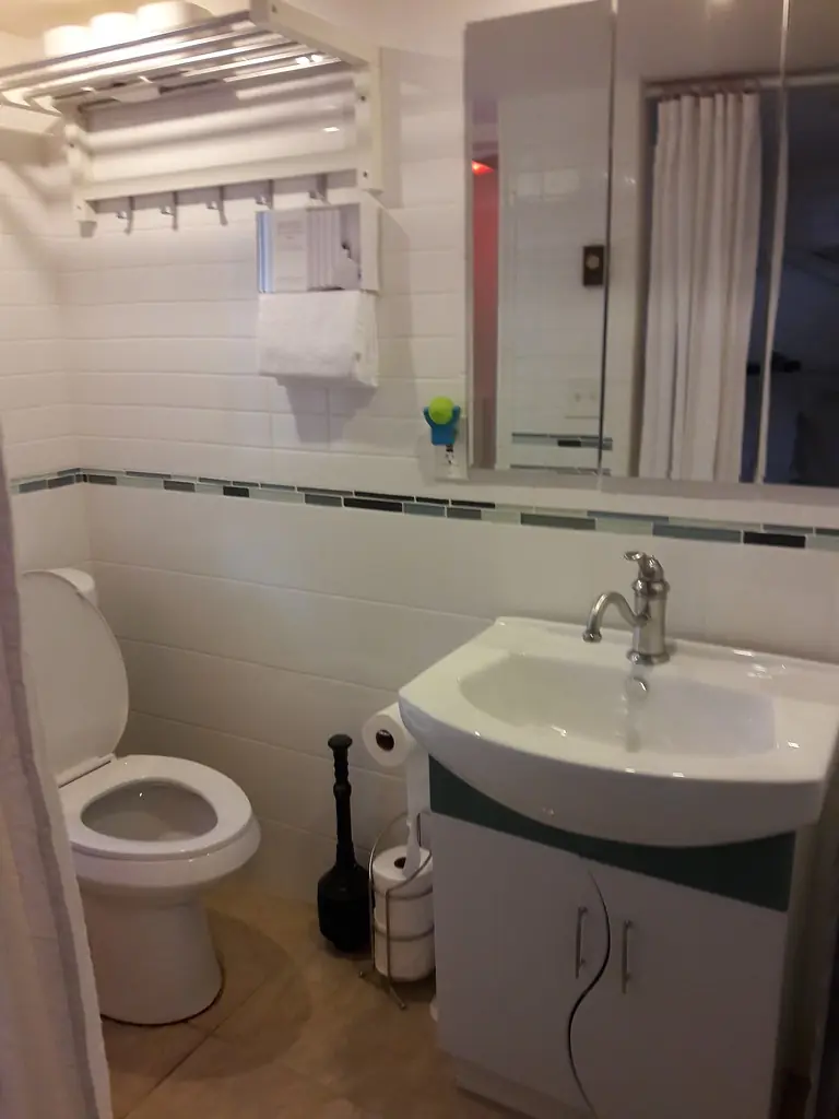 A white tiled bathroom with toilet, basin and towel rack